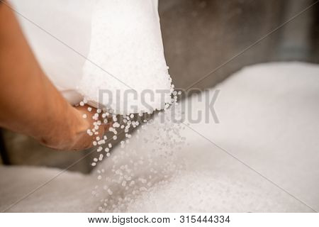 Small plastic granules scattering out of white sack held by worker