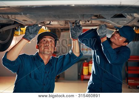 Professional Mechanics With Dirt On Faces Attaching Front Car Suspention After Diagnostics