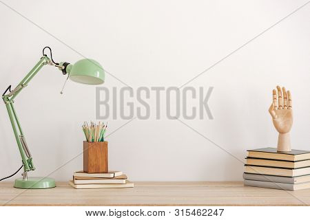 Pastel Mint Colored Lamp On Wooden Desk With Books, Copy Space On Empty White Wall