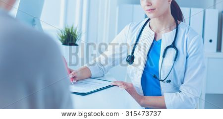 Doctor and patient discussing medical problems in a hospital consulting room. Doc filling in a patient's form