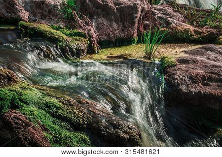 Close-up Of A Stream In Stones. Stones With Green Moss And Grass.
