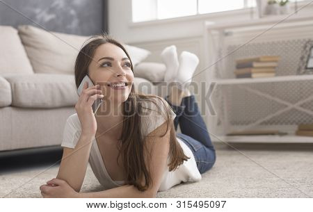 Cheerful Girl Laying On Floor And Talking On Cellphone At Home, Copy Space