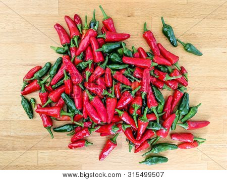 Red And Green Chilli Peppers. Large Fresh Pile On A Wooden Kitchen Worktop. Overhead View.