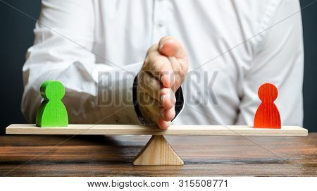 A Man Divides With His Palm Two Figures Of People Of Opponents On The Scales. To Reason And Settle T