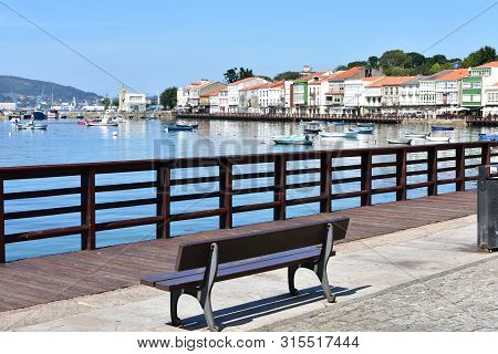 Mugardos, Spain. August 2, 2019. Small Fishing Village With Boardwalk And Wooden Bench. Blue Sky, Su
