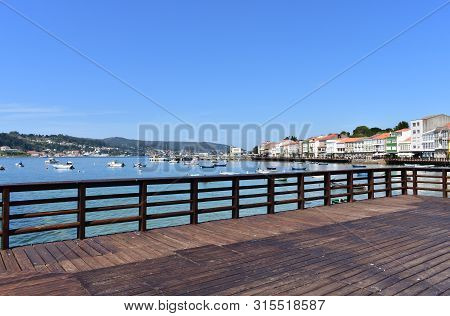 Mugardos, Spain. August 2, 2019. Small Fishing Village With Wooden Boardwalk And Handrail. Blue Sky,