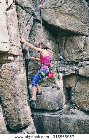 The Girl Climbs The Rock. Rock Climber Is Training On Natural Terrain. Extreme Hobby. A Woman Overco