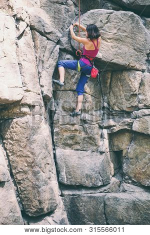 The Girl Climbs The Rock. Rock Climber Is Training On Natural Terrain. Extreme Hobby. A Woman Overco