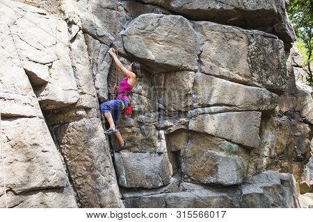 The Girl Climbs The Rock. Rock Climber Is Training On Natural Terrain. Extreme Hobby. A Woman Overco