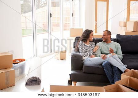 Couple Taking A Break And Sitting On Sofa Celebrating Moving Into New Home With Champagne