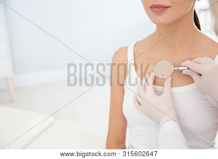 Dermatologist Examining Patient's Birthmark With Magnifying Glass In Clinic, Closeup. Space For Text