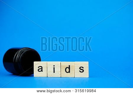 The Word Aids On Wooden Cubes And A Medical Dark Flask On A Blue Background. Medical Concept On Anti