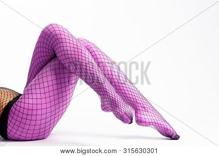 Close-up Of Slim Legs Of A Beautiful Woman In Nylon Purple Tights In A Mesh Posing In An Elegant Pos