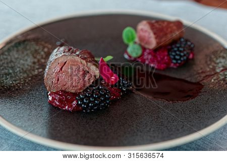 Venison fillet with beetroot carpaccio and blackberries on dark plate
