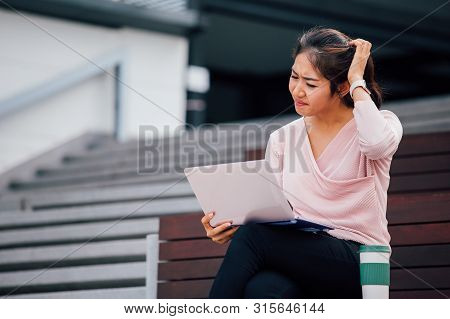 Young Asian Girl Having Headache And Scatching Her Head With Laptop On Her Lap In University Campus 