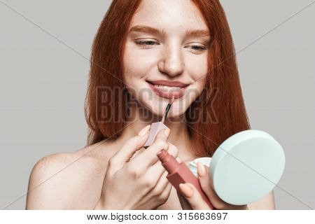 Making Beauty. Portrait Of Cute Young Woman With Long Red Hair Painting Lips With Lipliner And Looki