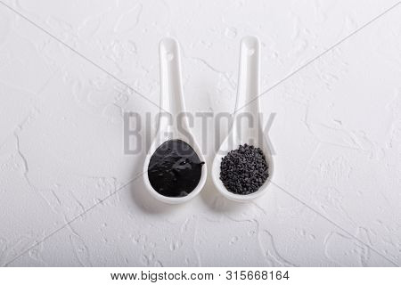 Black Tahini Sauce And Black Sesame Seeds In Spoons On White Background. Natural Paste Made From Ses