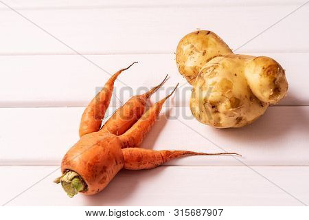 Flat Lay Ugly Curved Ogranic Carrot And Potato On White Wooden Background.