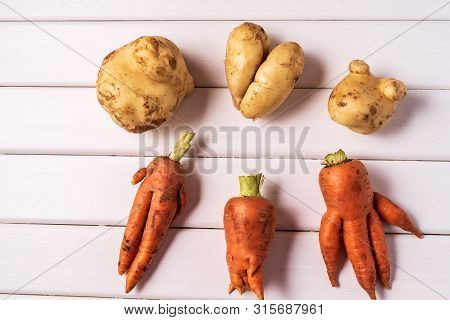 Flat Lay Some Ugly Curved Ogranic Carrots And Potatoes On White Wooden Background.