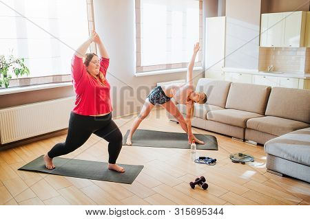 Young Slim And Overweight Models Exersicing Together In Living Room. Standing In Asana Or Yoga Poses