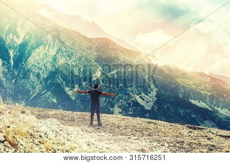 Young Man Standing On Top Of Cliff In Summer Mountains At Sunset And Enjoying View Of Nature In Llog