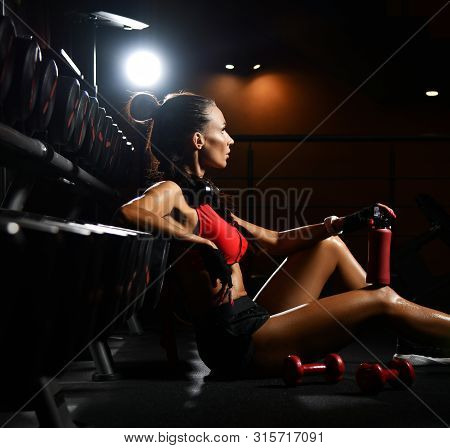 Athletic Woman Has A Break From Working Out Is Sitting On The Floor At Stand With Dumbbells With Her