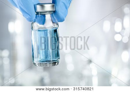 Healthcare concept with a hand in blue medical gloves holding a vaccine vial with blue liquid