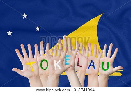 Inscription Tokelau On The Children's Hands Against The Background Of A Waving Flag Of The Tokelau