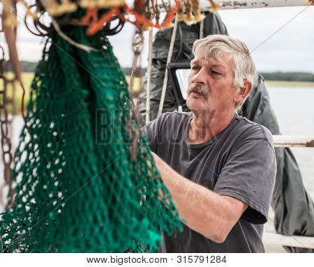 BEAUPORT, SOUTH CAROLINA-SEPTEMBER 14, 2015: A weathered commercial fisherman mends a net on a boat off the coast of South Carolina.