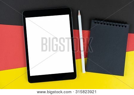 Black Tablet, E-book, Notebook And White Pencil Is On Flag Germany. Texture Deutsch National Flag Co