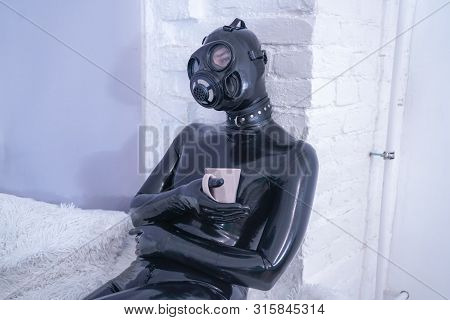 Morning Cup Of Tea Breakfast. Fetish Male In Rubber Black Suit At White Windowsill.
