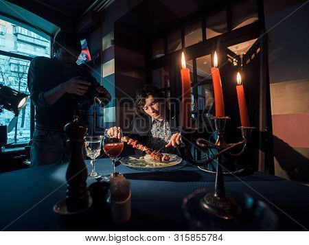 Photographer Shoots A Businessman-model In A Restaurant At The Table. Rich Man Advertises Clothes. P