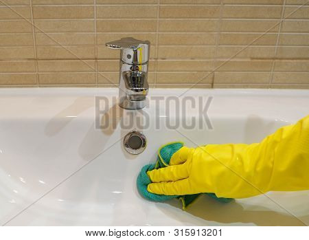 Woman In Yellow Rubber Gloves Cleaning A White Water Sink. Housewife Holding A Green Rag. Modern Bat
