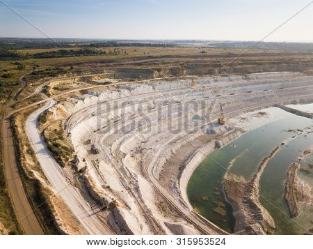 Opencast mining quarry with machinery at work - Aerial view. Industrial Extraction of lime, chalk, calx, caol. View from above