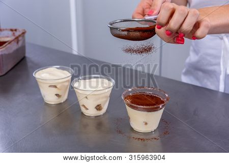 Pastry Chef In The Kitchen Makes Tiramisu With Raspberries. Cook Sprinkles Cocoa On A Prepared Desse