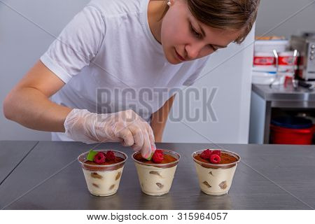 Pastry Chef In The Kitchen Makes Tiramisu With Raspberries. Cook Puts The Pieces Of Chocolate On The