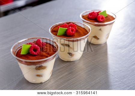 Pastry Chef In The Kitchen Makes Tiramisu With Raspberries And A Slice Of Chocolate. Finished Desser