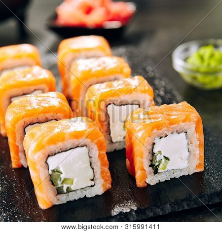 Beautiful Philadelphia Sushi Rolls Set with Salmon and Cream Cheese and Cuccumber on Black Slate Plate Close Up. Uramaki, Nori Maki or Futomaki Sushi with Trout Fillets, Soy Sauce and Wasabi