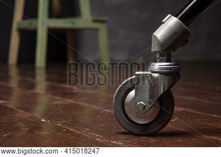 Ride On A Chair Leg With Tangled Hair On The Wooden Floor. Dirt Stuck To The Wheel. Close-up.