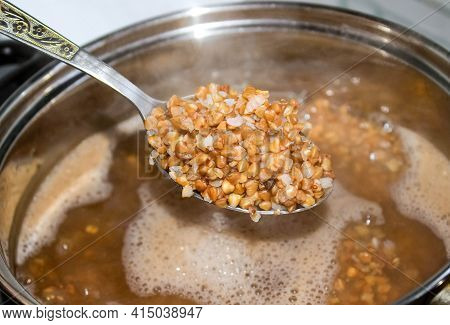 Buckwheat In A Spoon On The Background Of A Pan With Buckwheat Groats. Close-up, Selective Shot.