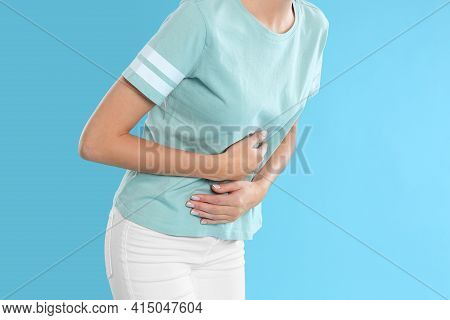 Woman Suffering From Stomach Ache On Light Blue Background, Closeup. Food Poisoning