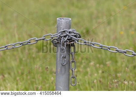 Industrial Chain Attached To A Galvanised Fence Post In A Green Field