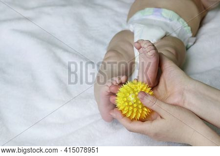 Moms Hands Are Massaging The Babys Legs With A Yellow Rubber Ball With Sharp Spikes. Fitness With Ch