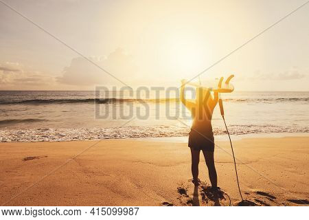 Woman Hold Surfboard Standing At Tropical Sunset Beach Background. Summer Vacation And Sport Adventr