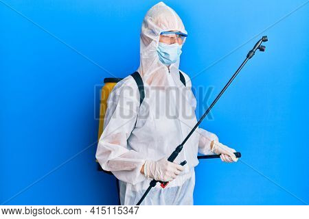 Covid specialist wearing decontamination protective suit and disinfectant spray, decontaminate and sanitize surface, standing over blue background