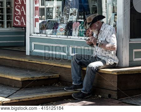 Key West, Usa - 04.30.2017: An Old Stylish Man In Cowboy Hat With Epic White Beard Sitting On A Wood
