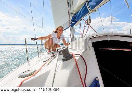 Young Woman Sailing On A Yacht. Female Sailboat Crewmember Trimming Main Sail During Sail On Vacatio