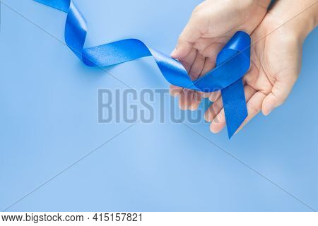 Hands Holding Deep Blue Ribbon On Blue Background With Copy Space. Colorectal Cancer Awareness Colon