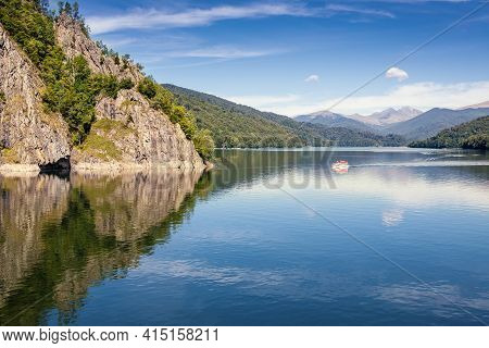 Daylight View To Vidraru Lake In Carpathian Mountains. Bright Blue Sky And Green Trees. Boat Cruisin