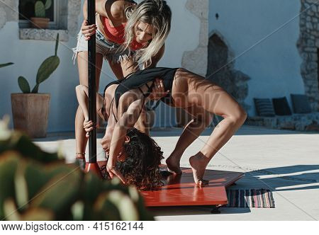 Instructor Helping Young Pole Dancer In A Black Swimsuit To Take A Pose On A Portable Platform Again